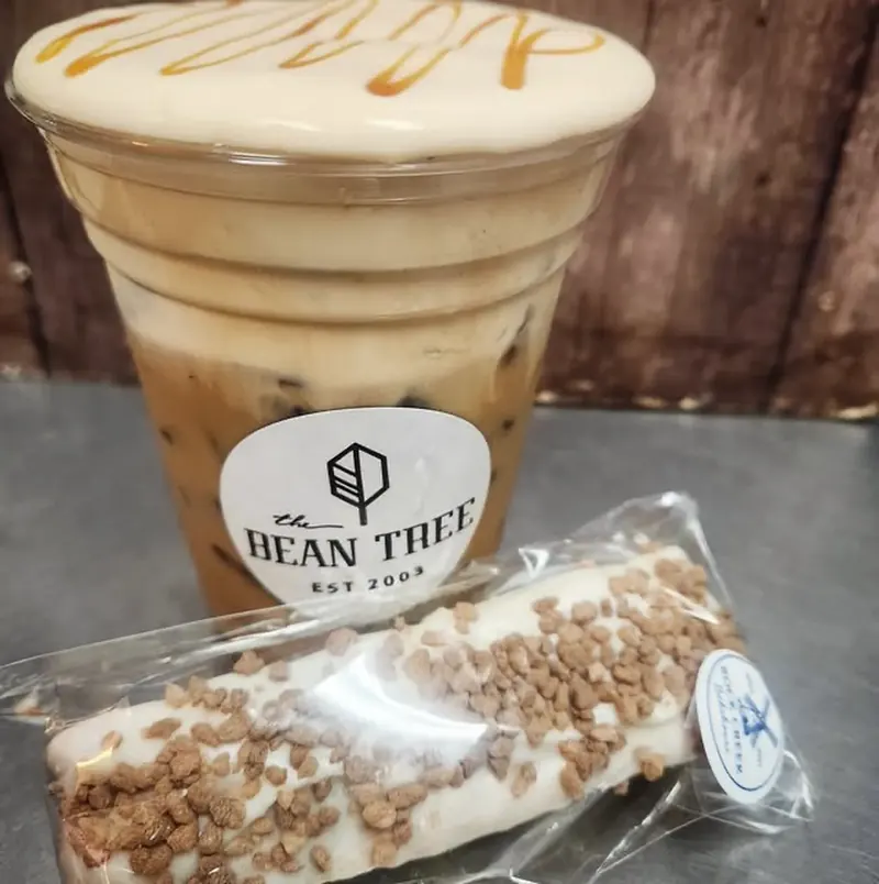 Layered iced latte with cold foam and caramel drizzle beside a wrapped toffee-topped treat