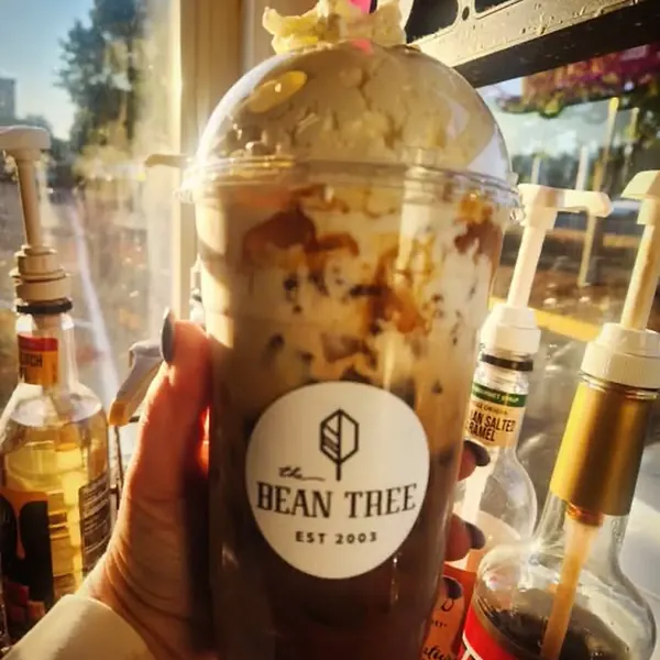 Iced mocha with whipped cream glowing in golden-hour light among syrup bottles, in a Bean Tree cup